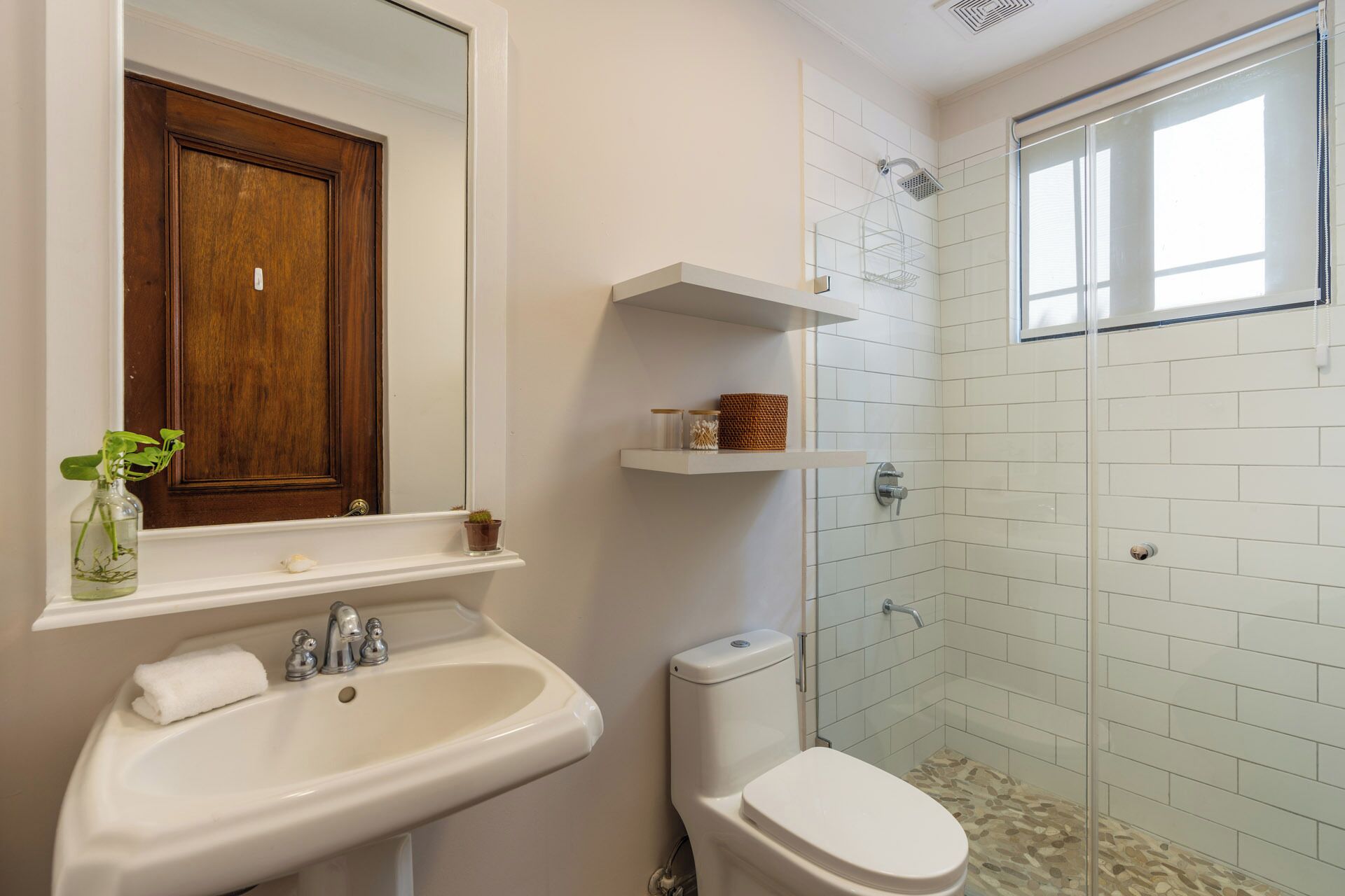 Une salle de bain avec un lavabo blanc, des toilettes, une porte en bois et un espace douche doté d’une porte en verre.