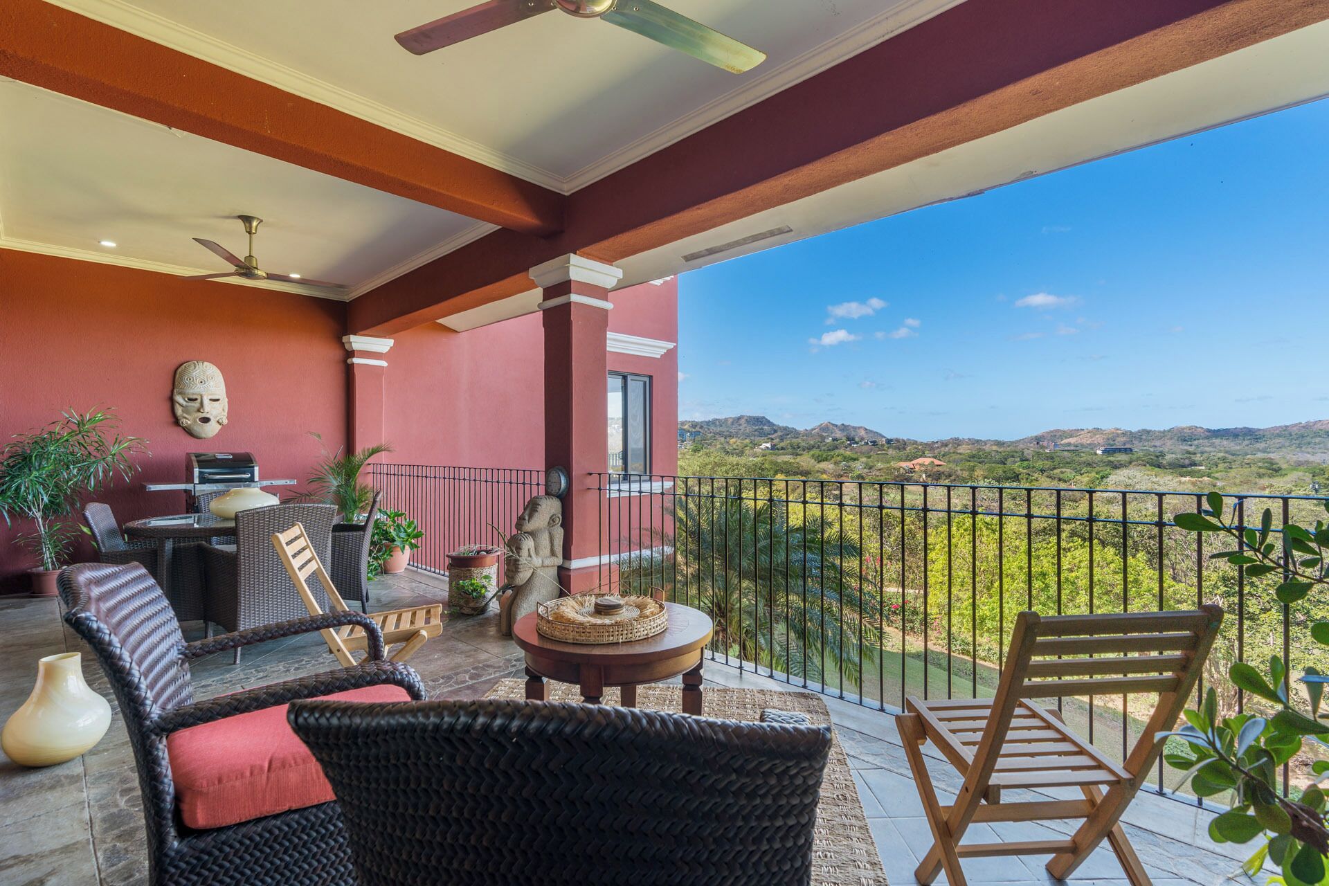 A balcony with wicker furniture, a grill, and a view of the landscape.