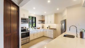 A modern kitchen with white cabinetry, stainless steel appliances, and a large window.