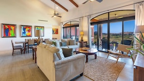 A spacious living room with a large window, ceiling fan, and artwork on the walls.