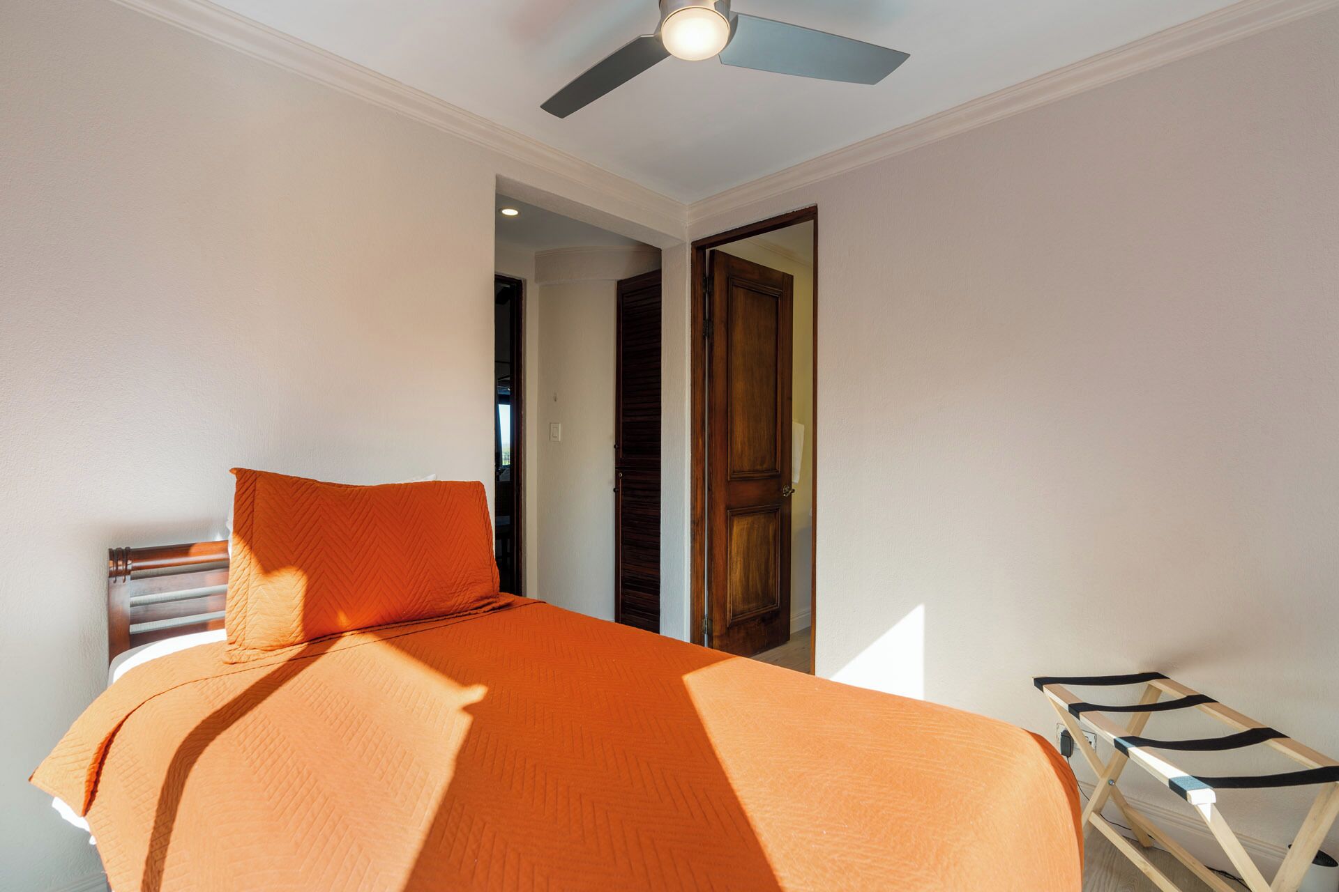A bedroom with a bed, a ceiling fan, and a door leading to another room.