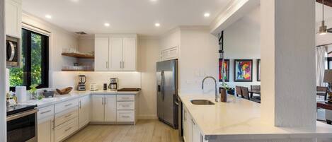 A modern kitchen with white cabinetry, stainless steel appliances, and a large island with a sink.