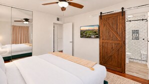 A bedroom with a bed, a ceiling fan, a sliding barn-style door, and a bathroom with a shower and toilet.