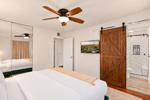 A bedroom with a bed, a ceiling fan, a sliding barn-style door, and a bathroom with a shower and toilet.