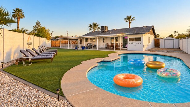 A backyard with a swimming pool, lounge chairs, and a covered patio area.
