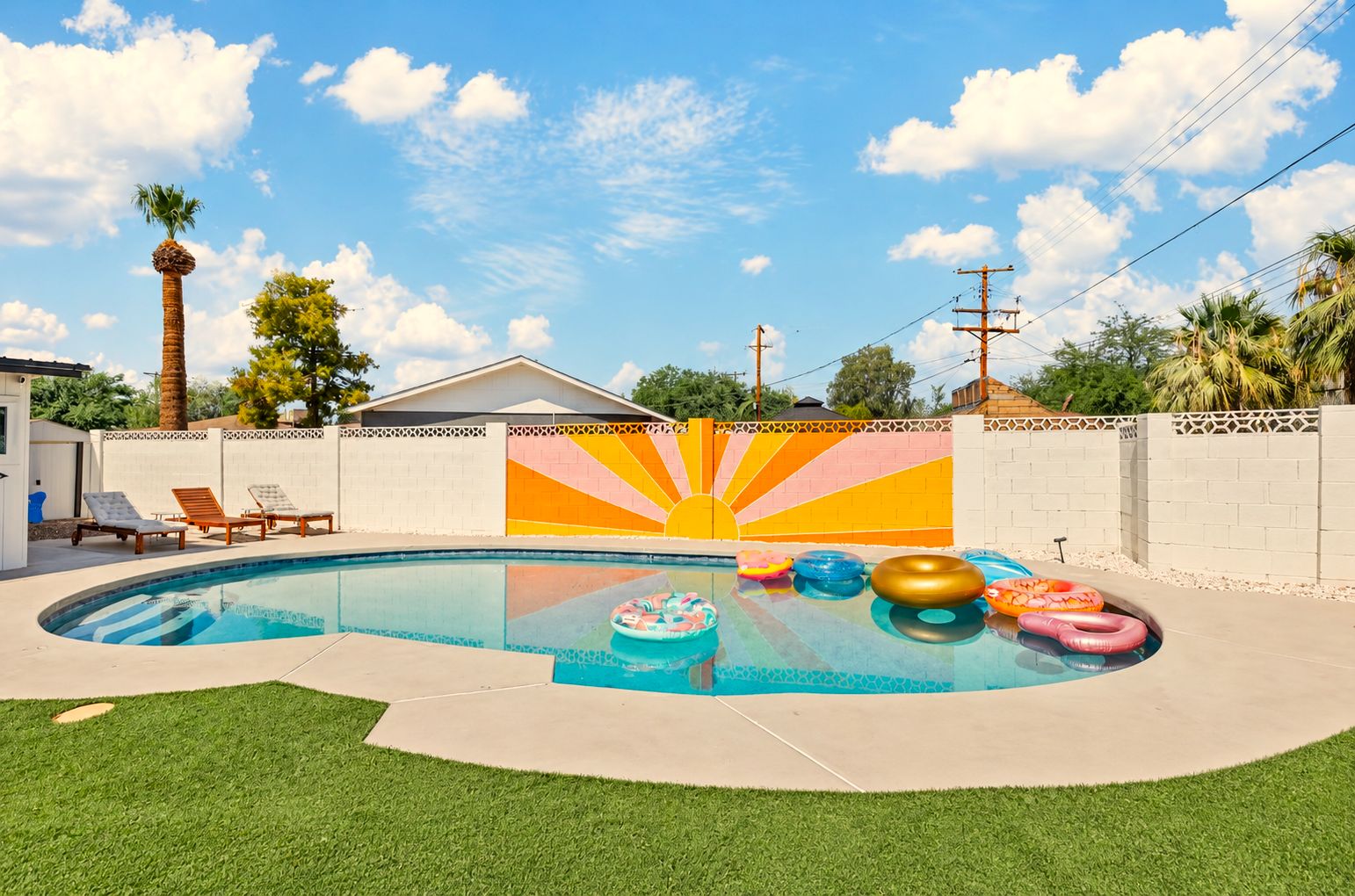 Una piscina con flotadores, un mural de sol y una casa al fondo.