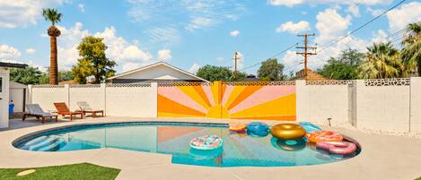 A swimming pool with inflatable rings, a sun mural, and a house in the background.