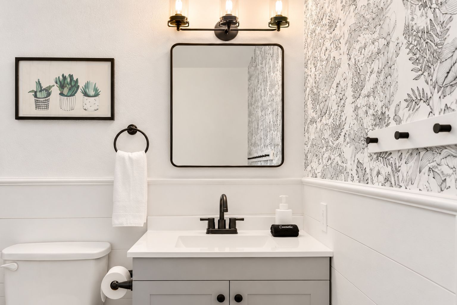 Une salle de bain avec un meuble-lavabo blanc, un robinet noir, des toilettes et une illustration botanique encadrée.