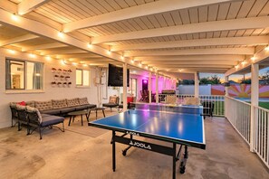 An indoor ping pong table with a sofa and chairs nearby, a ceiling with exposed beams, and a wall with potted plants. - The Pine Desert Retreat - Scottsdale's Ultimate Getaway (Scottsdale)