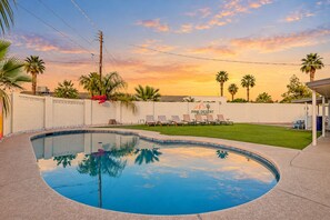 A swimming pool with a curved edge, surrounded by a white wall and palm trees. There are lounge chairs and a covered area with a sign that reads 'Pine, Desert Resort.'