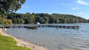 A pier extending into a lake with a grassy shoreline and a forested hill in the background. - Amazing home in Prokowo with sauna (Prokowo)