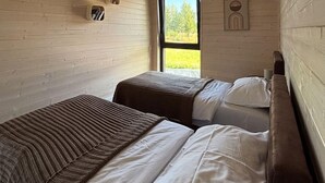 A room with two beds, one with a striped blanket and the other with white bedding. There is a window with a view of trees and a door with a circular handle. - Awesome home in Sianowo with WiFi (Sianowo)