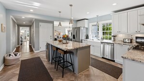 A modern kitchen with a central island, bar stools, stainless steel appliances, and a view to the outdoors. - Hot Tub • Fenced Yard • Perfect Family Retreat Near Chagrin Falls (Geauga County)
