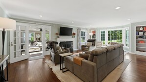 A spacious living room with a fireplace, a large sofa, a television, and a bookshelf. - Hot Tub • Fenced Yard • Perfect Family Retreat Near Chagrin Falls (Geauga County)