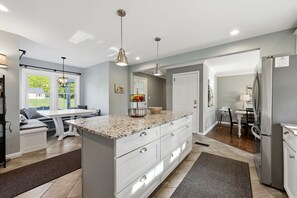 A modern kitchen with a large island, pendant lighting, and a view to the outside.