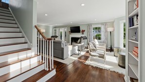 A spacious living area with a staircase, a fireplace, and a bookshelf. - Hot Tub • Fenced Yard • Perfect Family Retreat Near Chagrin Falls (Geauga County)