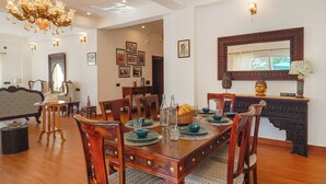 A dining area with a wooden table set for four, surrounded by chairs. There is a chandelier above the table, and a large mirror on the wall. - amã Stays & Trails White Hackle, Dharamshala (Dharamshala)