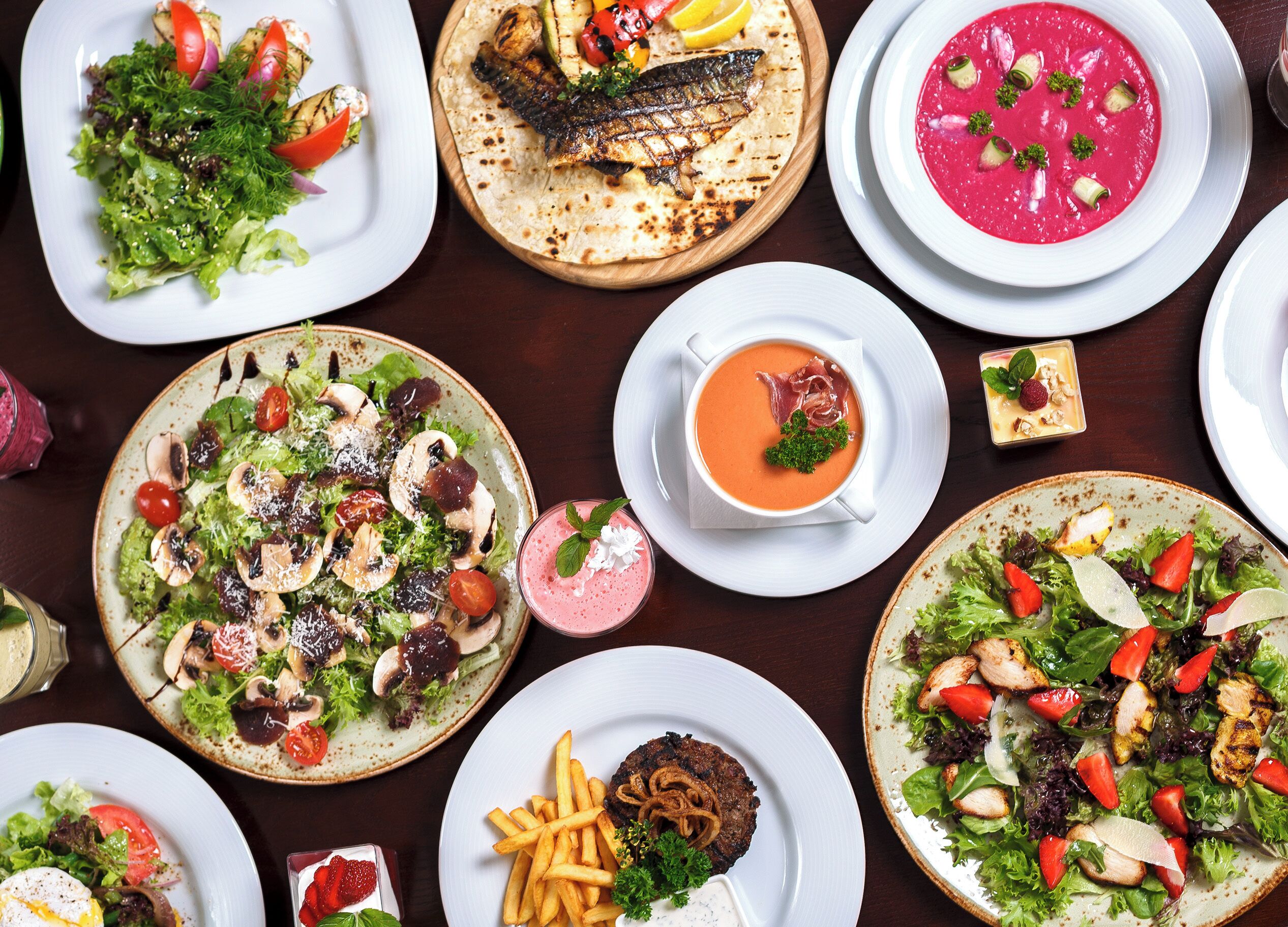 Variedad de platos que incluyen ensaladas, pescado a la parrilla y un tazón de sopa, lo que sugiere una amplia selección de comidas.