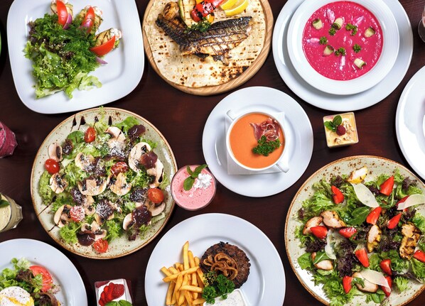 A variety of dishes including salads, grilled fish, and a bowl of soup, suggesting a diverse meal selection.