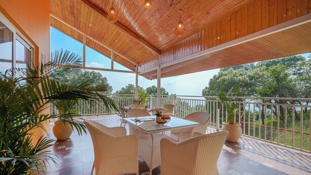 A covered outdoor dining area with a glass table, wicker chairs, and potted plants. - amã Stays & Trails White Hackle, Dharamshala (Dharamshala)