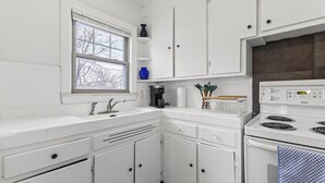 Una cocina con gabinetes blancos, una ventana, una cafetera y una estufa.