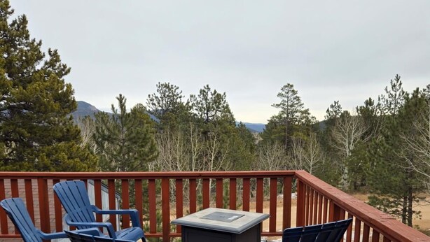 A wooden deck with blue Adirondack chairs and a small table, overlooking a forested area with mountains in the distance. - Welcoming 2-bedroom house in Bailey perfect for your getaway. (Bailey)