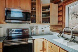 A kitchen with wooden cabinets, a stainless steel microwave, a Samsung oven, a sink, and a window with a view of trees. - Cozy Cabin Getaway Above Park City With Hot Tub (Summit County)