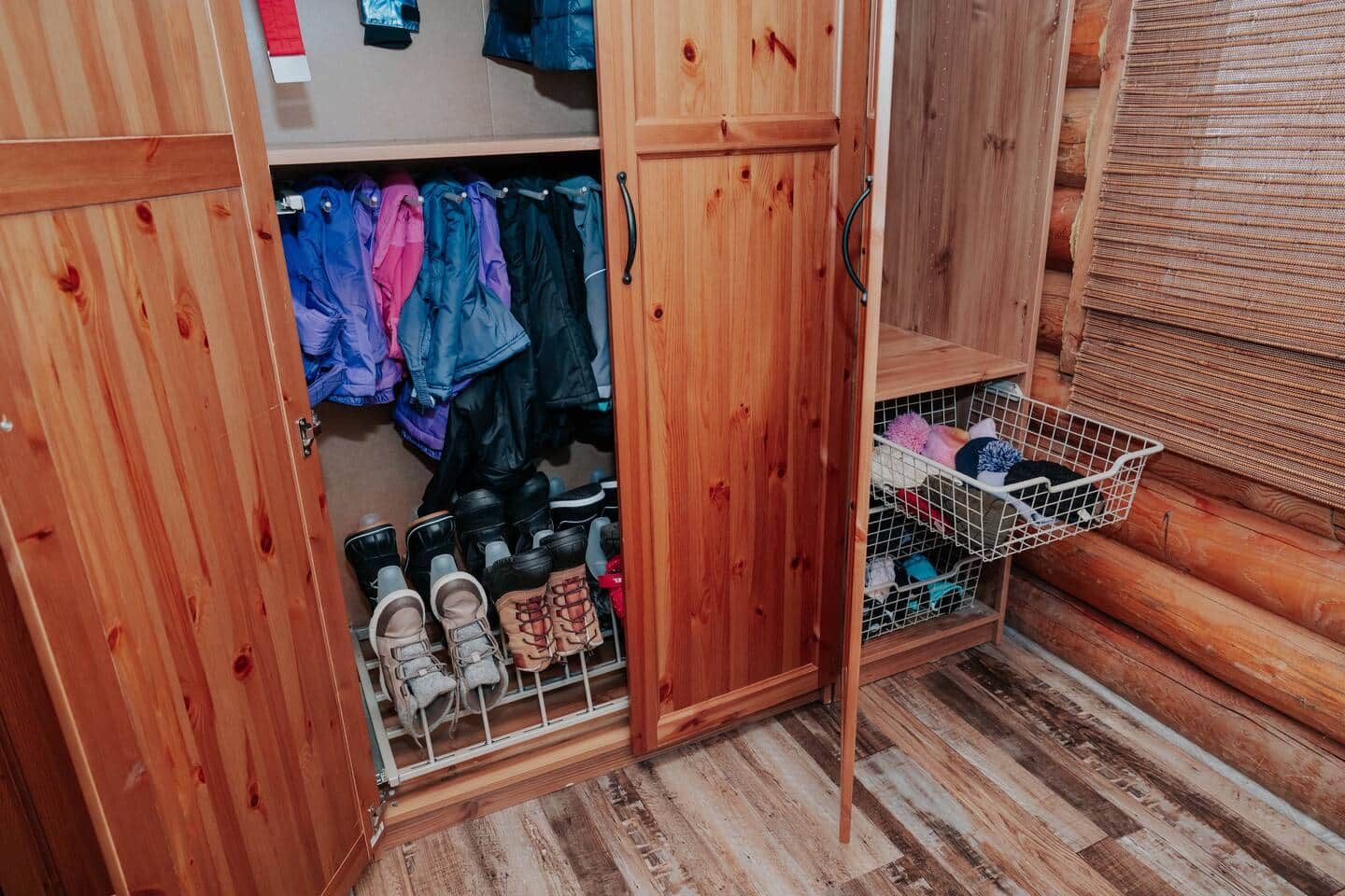 A wooden closet with hanging clothes and a shoe rack.
