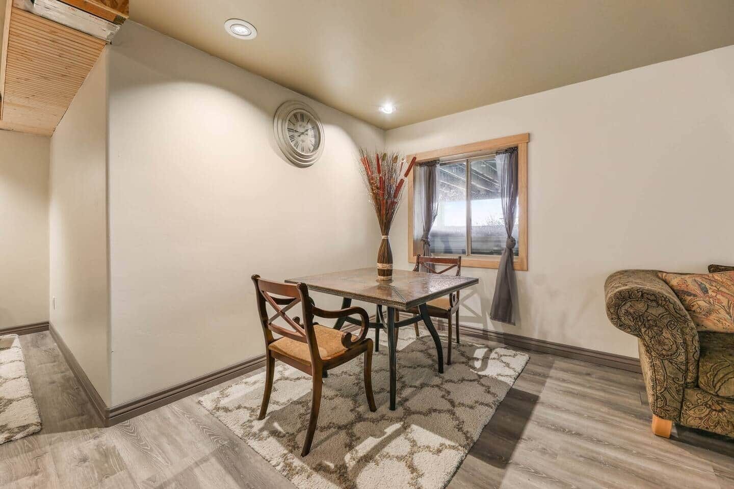 A dining area with a wooden table, chairs, and a vase of dried plants.