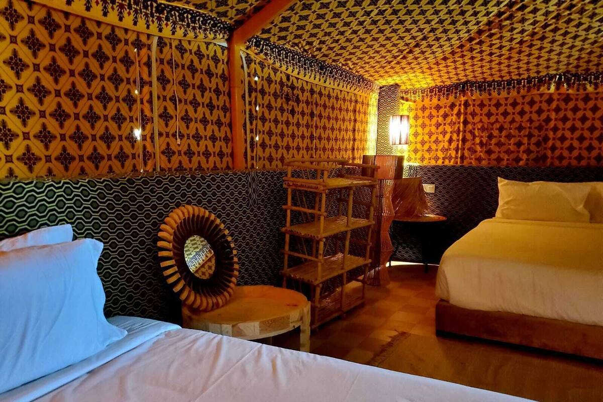 Una habitación con papel tapiz estampado, una cama, una silla y una pequeña mesa.