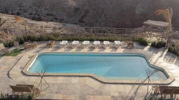 Piscina rectangular con solárium alicatado, rodeada de sillones blancos y una valla de madera.