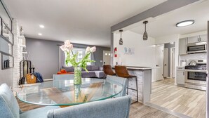 A modern kitchen with stainless steel appliances, a glass dining table, and a living area with a sofa and chairs.