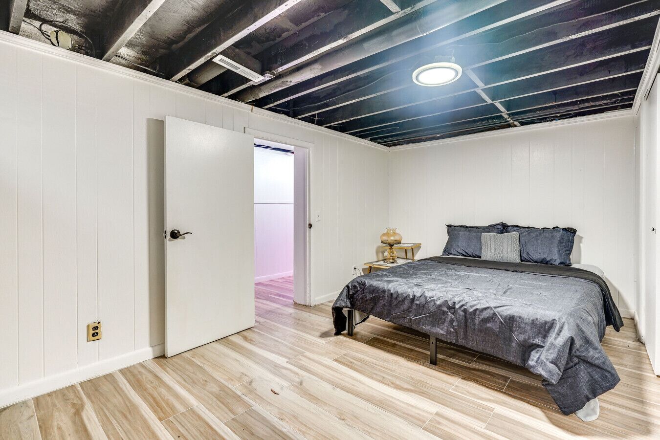 Um quarto com uma cama, uma mesa de cabeceira e uma porta que dá para outro cômodo.