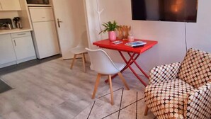 Un soggiorno moderno con un tavolo rosso, sedie bianche e un divano a fantasia. Un televisore a schermo piatto è montato sulla parete.