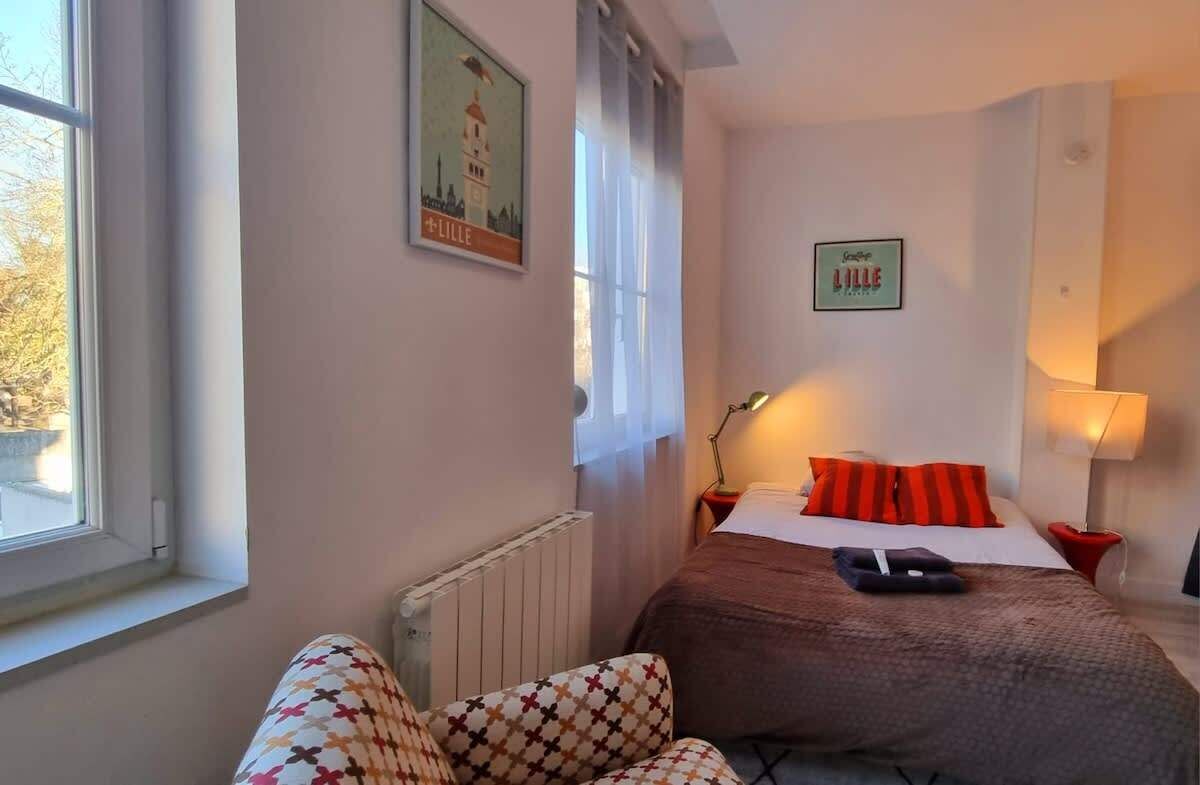 A hotel room with a bed, a chair, a nightstand, a lamp, and a poster on the wall.