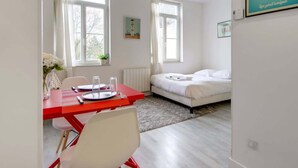 Una camera da letto moderna con un letto, un tavolo rosso con sedie e una finestra con tende.