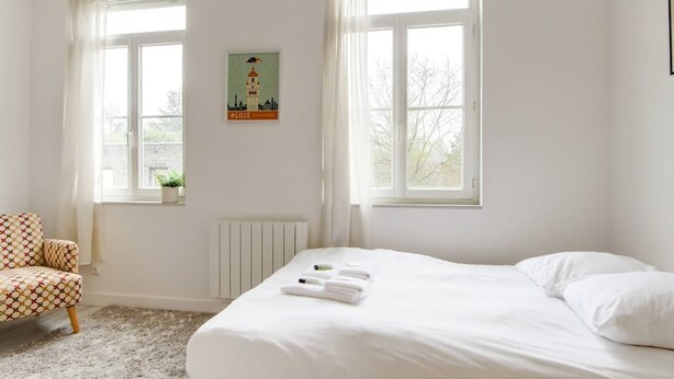 Una camera da letto con un letto, una sedia, un termosifone e una finestra vista alberi.