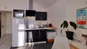 Une cuisine compacte équipée d’un four à micro-ondes, d’un évier et de meubles de couleur noire. On y trouve une plante en pot et un tableau encadré accroché au mur.