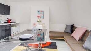 Un espace de vie compact comprenant un coin cuisine, un coin repas et un canapé avec des coussins.