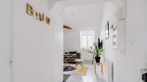 Un couloir moderne et bien éclairé qui mène à un espace de vie comprenant un canapé, une table basse et une plante en pot.