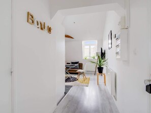 Corredor moderno e bem iluminado que dá para uma sala de estar com sofá, mesa de centro e um vaso de planta.