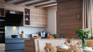 Une cuisine moderne avec des meubles en bois, un four encastré et un coin repas comprenant une table et des chaises en bois.