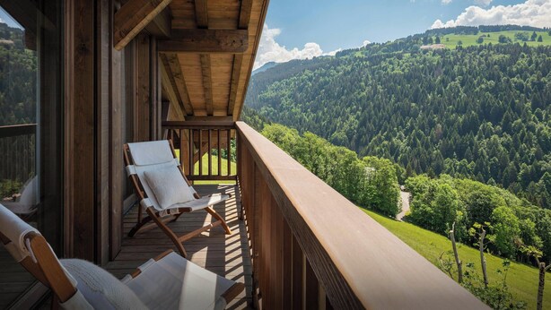 Un balcon en bois, agrémenté de deux fauteuils et d’un tableau, qui offre une vue sur une vallée boisée.