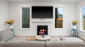 A living room with a fireplace, a flat-screen TV, and two side tables with flower arrangements. - ANCHORAGE HOUSE WITH PEACEFUL PLACE (Anchorage)