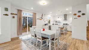 A modern kitchen with white cabinets, a central island, and a dining area with a striped tablecloth. - ANCHORAGE HOUSE WITH PEACEFUL PLACE (Anchorage)