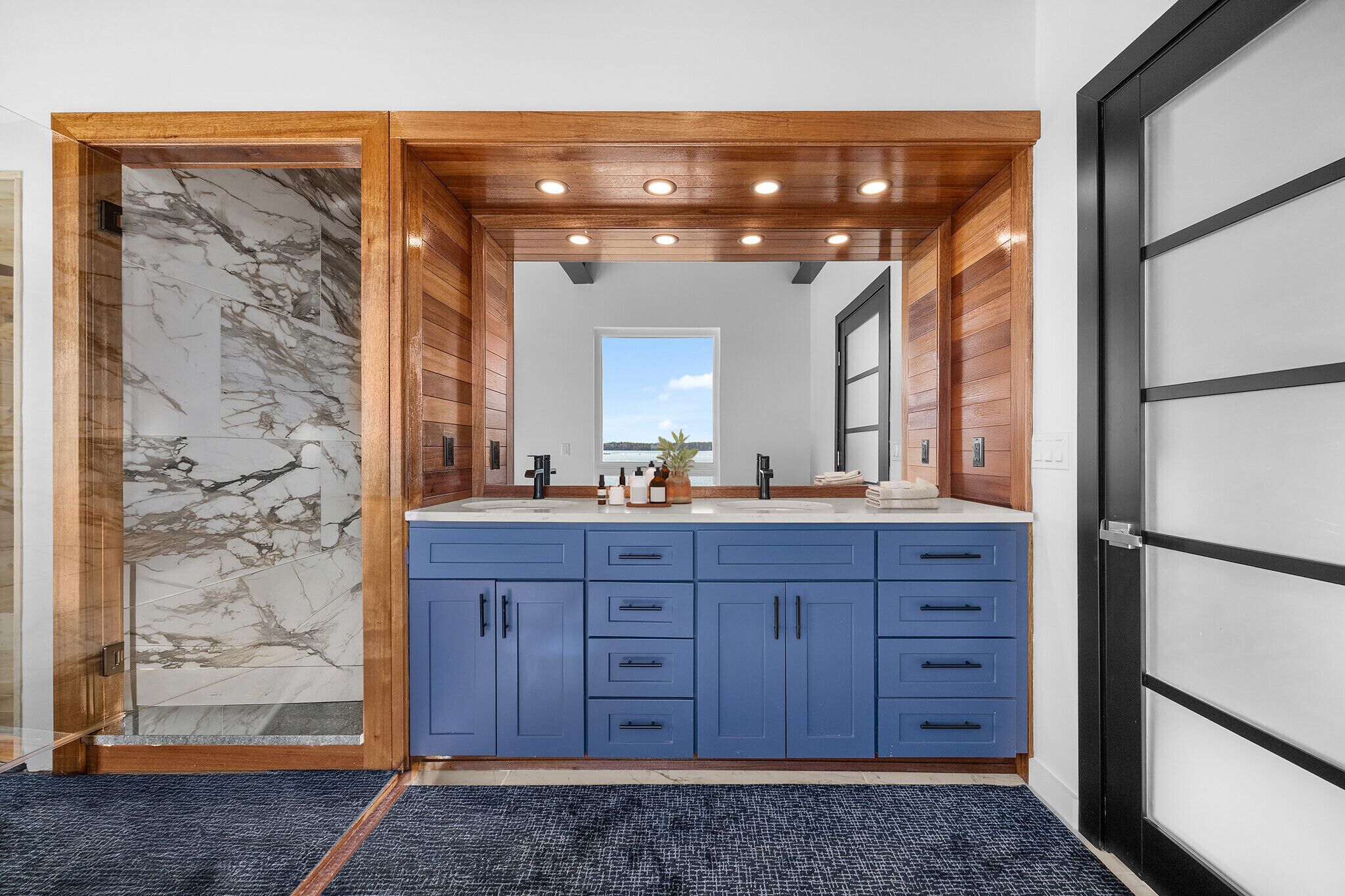 A modern bathroom with a marble vanity, wooden ceiling, and a large mirror.