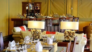 Ein Essbereich mit gedeckten Tischen, eine Bar mit Flaschen und eine Lounge mit Sofas und Sesseln.