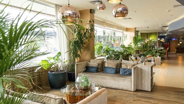 A modern hotel lobby with seating areas, large windows, and indoor plants. - Ibis Styles Curitiba Airport Hotel (Sao Jose dos Pinhais)