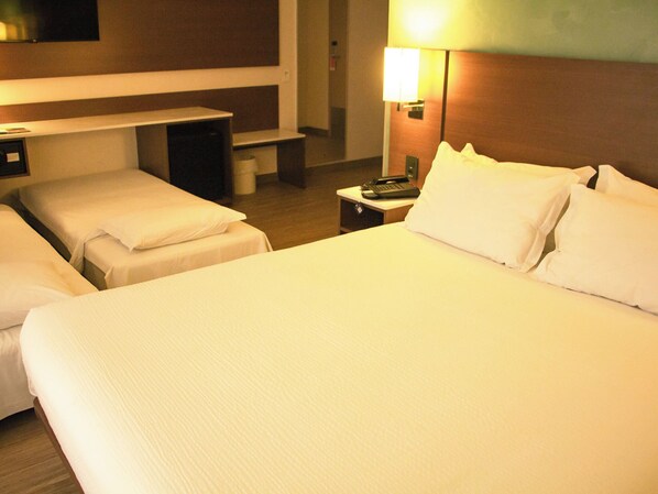 A hotel room with two single beds and a larger bed, a bedside table with a lamp, and a small desk with a telephone. - Ibis Styles Curitiba Airport Hotel (Sao Jose dos Pinhais)