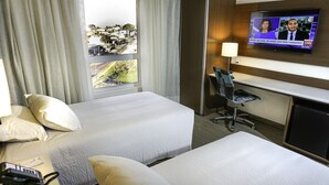 A hotel room with two beds, a desk, a TV, and a view of a cityscape. - Ibis Styles Curitiba Airport Hotel (Sao Jose dos Pinhais)